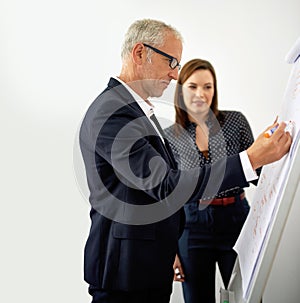 Passing on all his knowledge and experience. a mature businessman working on a whiteboard while a female colleague looks