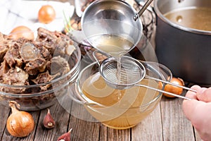 Passing the bone broth through a sieve. Concentrated Bone Broth in a bowl on the table