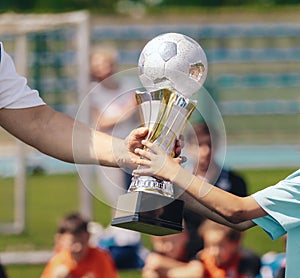 Passing of the Soccer Trophy Moment. Young Player Awarding Trophy Closeup. Child as a Team Captain Winning Sport Football Champion