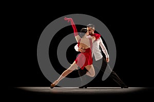 Passion and attraction. Young man and woman professional ballroom dancers dancing tango over black background. Concept