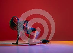 Passion, femininity. Portrait of young girl dancing heels dance over red background in neon with mixed light. Concept of