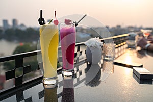 Passion fresh fruit juice with ice on outdoor table in cafe and bar. Pineapple and red dragon fruit. Urban lake on background