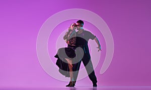 Passion. Man and woman, professional dancers in stylish, beautiful stage costumes performing tango over purple