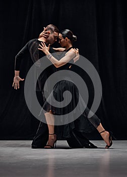 Passion, romance, emotions. Man and woman, professional tango dancers performing in black stage costumes over black