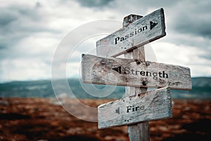 Passion, strength and fire text on wooden rustic signpost outdoors in nature/mountain scenery. photo