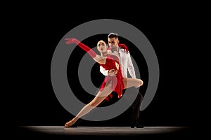 Passionate attractive young man and woman, professional ballroom dancers dancing tango over black background. Concept of