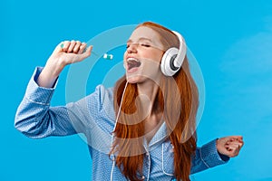 Passionate and carefree cute foxy european redhead woman in pyjama, close eyes wearing headphones, listening music