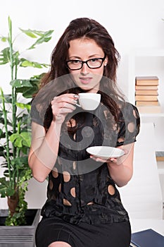 Passionate about coffee. Pretty woman drinking coffee in office. Sexy business woman with teacup sitting on desktop