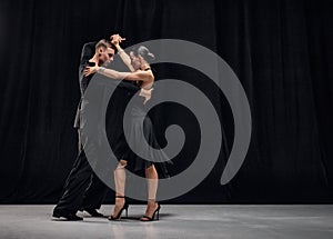 Passionate connection. Man and woman, professional tango dancers performing in black stage costumes over black