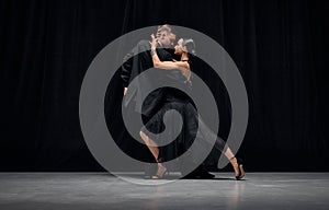 Passionate dance style. Man and woman, professional tango dancers performing in black stage costumes over black