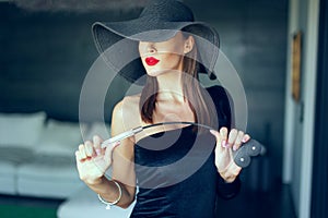 Passionate dominant femme fatale in hat with whip portrait