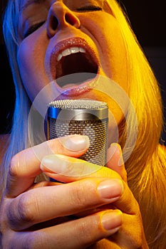 Passionate female vocalist under gelled lighting sings into condenser microphone