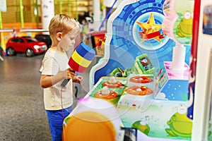 Passionate happy kid boy playing fun games on slot machine in amusement park