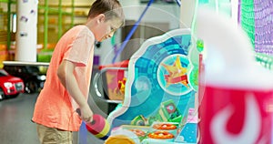 Passionate happy kid boy playing fun games on slot machine in amusement park