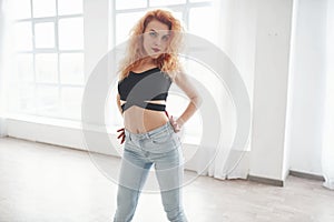 Passionate move. Attractive redhead woman posing in the spacey room near the window
