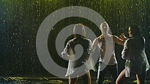 Passionate movements of a salsa dance in the rain on a dark smoky backlit background. A silhouette of three wet bodies