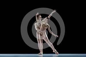 Passionate young couple, man and woman, ballet dancers in beige clothes dancing against black studio background