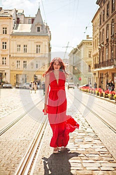 Passionate young girl, lady in long red dress on street of an old European city