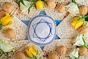 Passover celebration concept. Blue Star of David made from matzah, white and yellow roses, kippah and walnut on bluebackground.