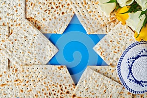 Passover celebration concept. Blue Star of David made from matzah, white and yellow roses, kippah and walnut on bluebackground.