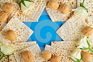 Passover celebration concept. Blue Star of David made from matzah, white and yellow roses, kippah and walnut on bluebackground.