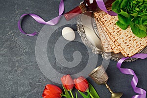 Passover holiday concept seder plate, matzoh and tulip flowers on dark background. Top view