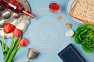 Passover holiday concept seder plate, matzoh, tulip flowers and wine bottle on wooden background.