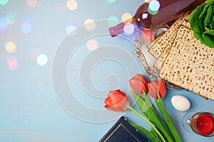 Passover holiday concept seder plate, matzoh and tulip flowers on wooden background with bokeh overlay. Top view