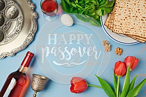 Passover holiday greeting card with seder plate, matzoh, tulip flowers and wine bottle on wooden background.