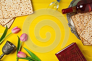 Passover Pesah celebration with matzoh, tulip flowers and wine bottle on yellow wooden background.