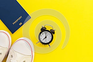 Passport, alarm clock and gum shoes on yellow background. Time to travel. Travel accessories. Holiday and vacation concept. Top