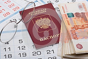 The passport of the Russian Federation lies on the background of calendar numbers, next to it lies a bundle of money and glasses