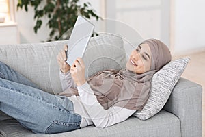 Passtime At Home. Relaxed Muslim Girl Lying On Couch With Digital Tablet