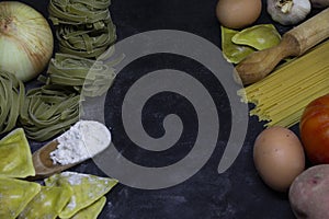 Pasta background with spaghetti , ravioli,eggs,onion,potato,garlic and a wood kneader on floury dark background.Italian cooking