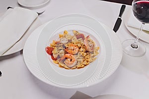 Pasta bavette with fried shrimps, bechamel sauce, mint leaf, garlic, tomatoes, chili on white plate, top view, italian