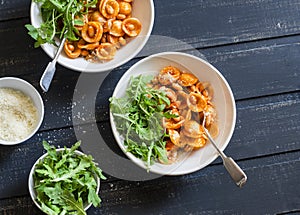 Pasta with beans, tomato sauce, parmesan and arugula on dark background, top view.