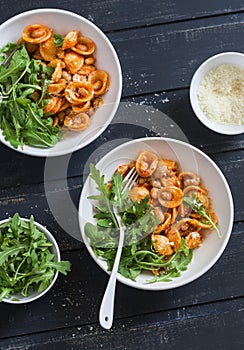 Pasta with beans, tomato sauce, parmesan and arugula on dark background, top view.