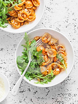 Pasta with beans, tomato sauce, parmesan and arugula on light background, top view