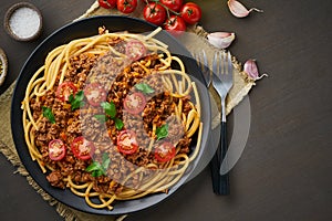 Pasta Bolognese bucatini with mincemeat and tomatoes, dark wooden background, top view, copy space