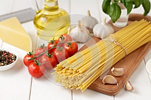 Pasta bucatini with tomatoes, garlic, cheese and oil on white wooden background.