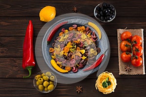 Pasta and burning peppers on a gray plate with tomatoes, sweet pepper, lemon, olives and olives on a wooden dark