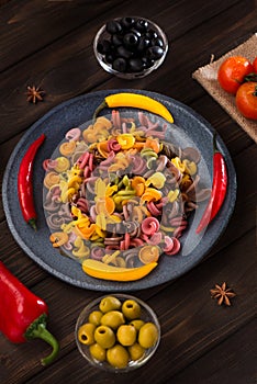 Pasta and burning peppers on a gray plate with tomatoes, sweet pepper, lemon, olives and olives on a wooden dark