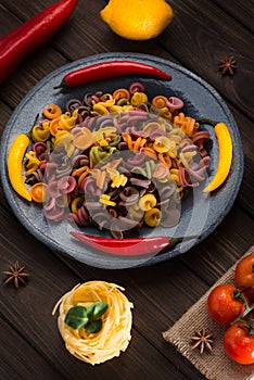 Pasta and burning peppers on a gray plate with tomatoes, sweet pepper, lemon, olives and olives on a wooden dark