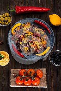 Pasta and burning peppers on a gray plate with tomatoes, sweet pepper, lemon, olives and olives on a wooden dark