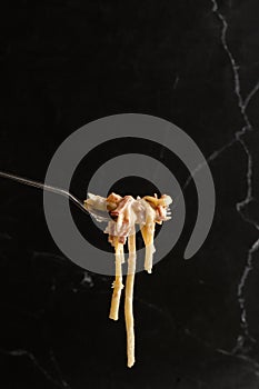 Pasta Carbonara on fork isolated. Spaghetti with bacon, parmesan, cream sauce and egg yolk on black marble background