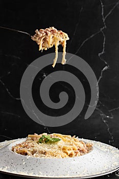 Pasta Carbonara on fork isolated. Spaghetti with bacon, parmesan, cream sauce and egg yolk on black marble background