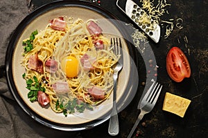 Pasta carbonara with parmesan, bacon, raw yolk and tomato on a dark rustic background. View from above