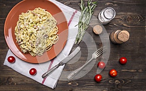Pasta carbonara with zucchini, in a brown plate with vintage knife and fork, with herbs and spices on rustic wooden background top