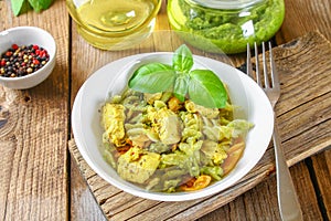 Pasta with chicken pieces and pesto sauce on an old wooden table.