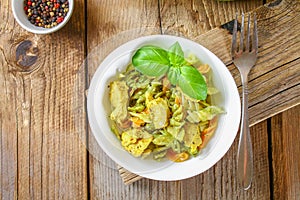 Pasta with chicken pieces and pesto sauce on an old wooden table.